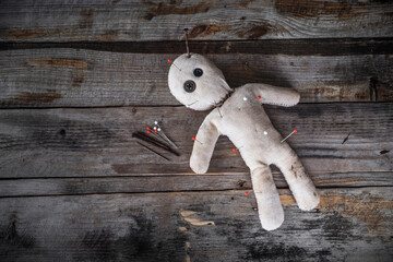 Creepy voodoo doll made from old cloth vintage style with pins from punishment stuck in body and a rusty nail stuck on head is lying on a wooden table in dark atmosphere background.