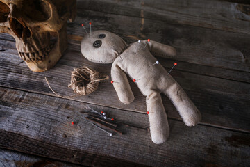 Creepy voodoo doll made from old cloth vintage style lying on wooden table with a skull with ritual equipment have rope, pins and rusty nails in dark atmosphere background.