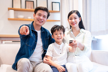 Happy Asian family smiles on the couch enjoying quality time together one points and other controls tv