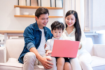 Asian family enjoys time together using a laptop on a sofa in a modern cozy living room