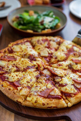 closeup scooping hawaiian pizza dough thick and soft with cheese pineapple ham and vegetable salad on wooden tray table for lunch to family eating food at italian pizza restaurant on vertical