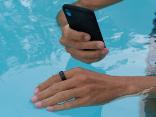 Hands in pool connect black smart ring health tracker to smartphone app.