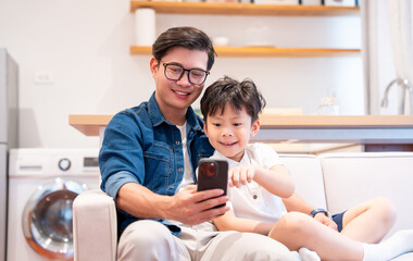 Father and son share quality time at home happily looking at a smartphone and smiling together