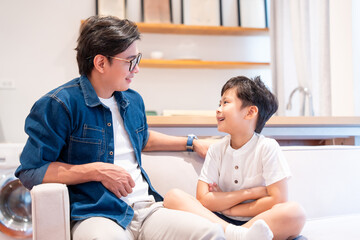 Father and son share a moment smiling at each other while sitting comfortably on a sofa