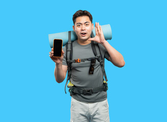Enthusiastic hiker showcases smartphone with blank screen on light blue backdrop ready for adventure