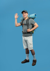 Friendly hiker waving on solid blue background Full shot of man ready for outdoor adventure