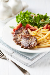 Grilled Steak with french fries and fresh salad. White wooden background.	