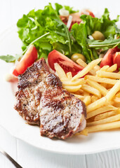 Grilled Steak with french fries and fresh salad. White wooden background.	