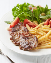 Grilled Steak with french fries and fresh salad. White wooden background.	