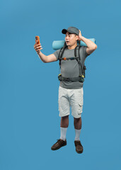 Surprised backpacker looking at phone with a look of concern against a blue studio background