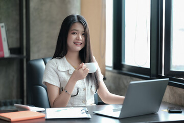 Fototapeta premium Portrait of a young woman drinking hot coffee in the morning at the office while thinking about a new business project.
