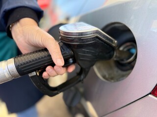 Close-up of a person refueling a car at a gas station, holding a fuel pump nozzle inserted into the...