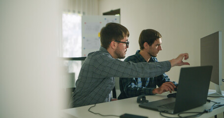 Obraz premium Two engineers work together at a desk in a modern lab, focusing on coding and development for a robotics project using laptops.