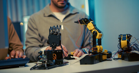 Close-up of engineers working on robotic arms in a modern tech workspace. Focus on hardware development, coding, and robotics prototyping.