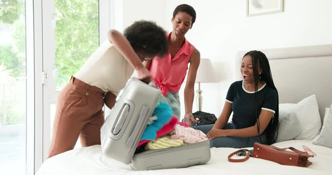 African American women friends pushing lid and tugging zipper to close full silver suitcase at home