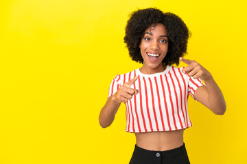 Young African American woman isolated on yellow background surprised and pointing front