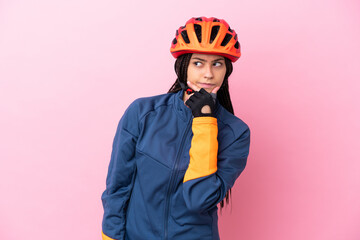 Teenager cyclist girl isolated on pink background having doubts