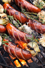 Grilled pork sausages, herbs, onion and garlic on a cast iron grill, close up view
