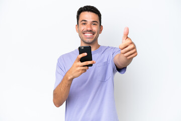 Young handsome man over isolated white background using mobile phone while doing thumbs up