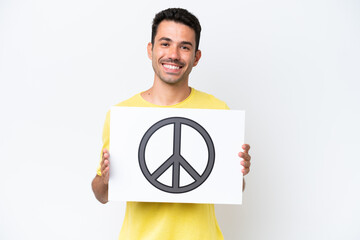 Young handsome man over isolated white background holding a placard with peace symbol with happy...
