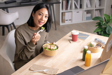 Asian woman eating healthy meal while working, Businesswoman having a lunch break at the office, Beautiful woman smiling and looking at camera while eating food