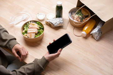 Asian woman eating healthy meal while working, Businesswoman having a lunch break at the office, hand holding phone with blank black screen for copyspace