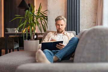Young businessman sitting on sofa at home and writing notes down on a notepad