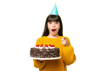Little girl holding birthday cake over isolated chroma key background surprised and pointing front