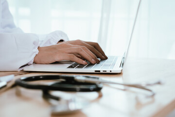 Focused female doctor working at her desk in a hospital, using a laptop and clipboard for patient consultation and diagnosis