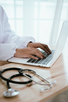 Focused female doctor working at her desk in a hospital, using a laptop and clipboard for patient consultation and diagnosis