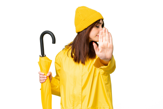 Young caucasian woman with rainproof coat and umbrella over isolated chroma key background making stop gesture and disappointed