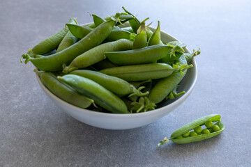 side view of green pea pods in white bowl on gray kitchen counter