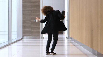 Energetic businesswoman dancing freely in corporate hallway, celebrating successful business deal while holding laptop and coffee cup with infectious joy and confidence