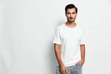 Smiling young man standing relaxed in a plain white t-shirt, casually posing with hands in pockets,...