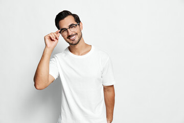 Smiling man wearing glasses poses confidently while adjusting his eyewear with a cheerful expression on his face against a solid white background. Lifestyle concept