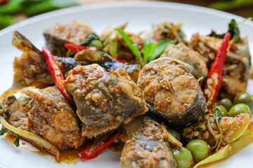 Spicy stir-fried catfish (Pad Cha Pla Dook) on a white plate, a popular and flavorful Thai dish. The dish features pieces of catfish stir-fried with herbs, spices, chili peppers and Original Thai food