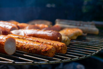 Grill loaded with sausages and marinated chicken, sizzling over hot charcoal, with smoke rising in the sunlight.