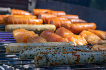 Raw marinated chicken breasts and sausages on a hot charcoal grill, ready for barbecuing.
