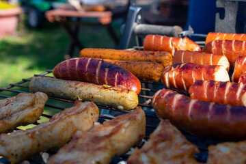 Grilled chicken pieces and sausages cooking over hot charcoal on an outdoor barbecue, with golden sear marks and a rustic metal grill.