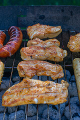 Grilled chicken pieces and sausages cooking over hot charcoal on an outdoor barbecue, with golden sear marks and a rustic metal grill.