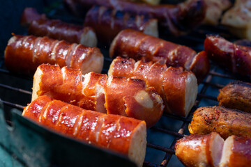 Grill loaded with sausages and marinated chicken, sizzling over hot charcoal, with smoke rising in the sunlight.