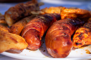 Close-up of grilled meat skewers and sausages on a white plate, served outdoors on a sunlit table, perfect for a summer barbecue.
