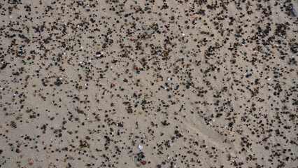 Sand covered with colorful pebbles and small shells along the beach in bright daylight with clear blue skies