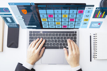 Hands typing on laptop with digital calendar and virtual interface on office desk from top view perspective.