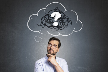 Thoughtful man standing against dark wall background with a drawn cloud containing a question mark symbolizing confusion or curiosity.
