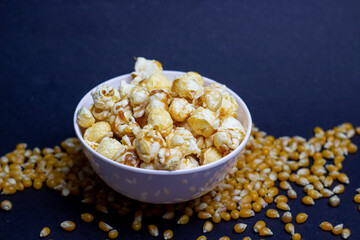 Sweet caramel popcorn in a bowl, surrounded by corn kernels. Perfect treat for movie nights and snacks