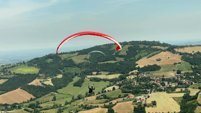 Sestola, Italy &ndash; 05 31 2025: Paraglider flies in the air. Aerial view of paragliding. Paraglider flies above the mountains in a bright sunny day. Concept of extreme sport.
