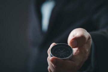 A hand holds a compass, symbolizing direction and guidance, set against a dark background.