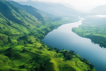 Obraz premium Lush green hills and calm lake create serene landscape with misty mountains in the background, Lush green hills and a calm lake with misty mountains in the distance, aerial view