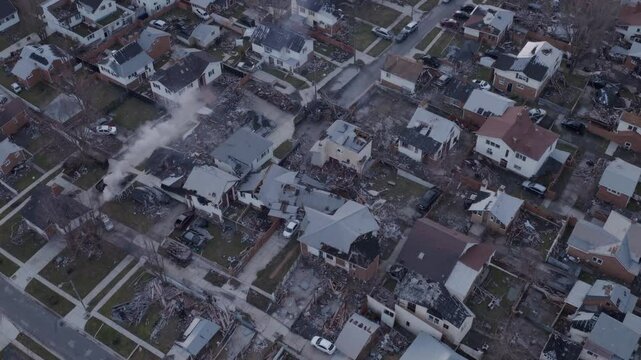 Aerial view of a suburban neighborhood showing damaged houses and debris. The scene captures the aftermath of a disaster, with scattered rooftops and empty lots.